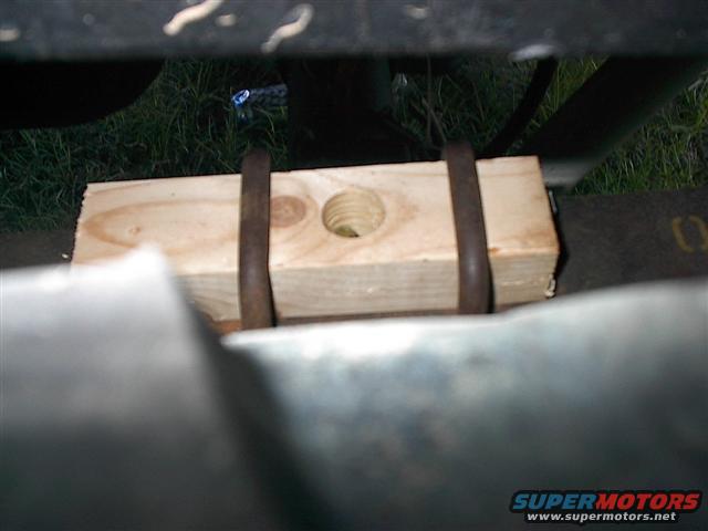 Wooden block held by metal straps under a vehicle part