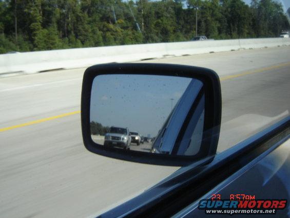 Side mirror view of two trucks on a highway