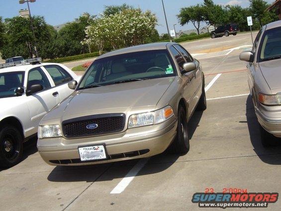Gold Ford Crown Victoria parked next to a white police car. Texas license plate visible