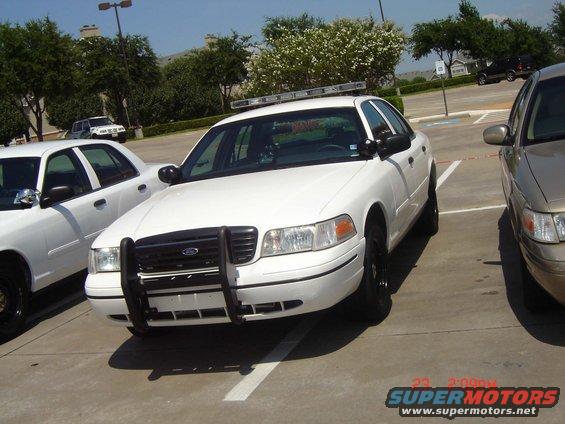 White police car with a push bumper and light bar, parked in a lot
