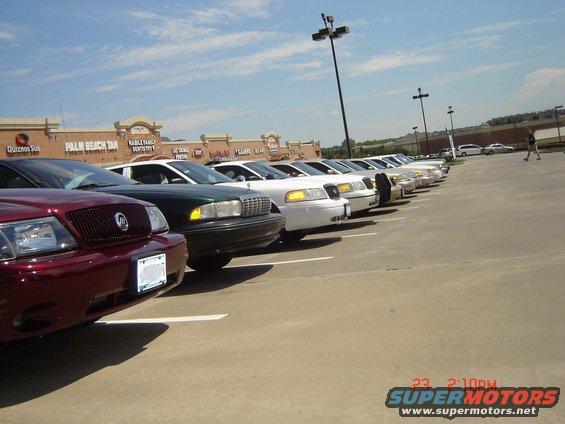 Several police cars and other vehicles parked in a lot. A sign at the bottom says SUPERMOTORS.NET