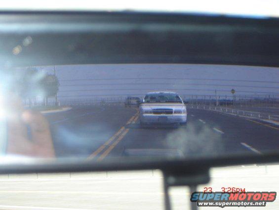 1992 Ford Crown Victoria driving on highway, seen in rearview mirror. Another car is visible ahead