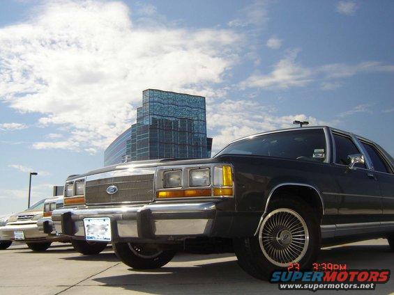 Dark sedan parked in front of a modern building, with another car visible behind it