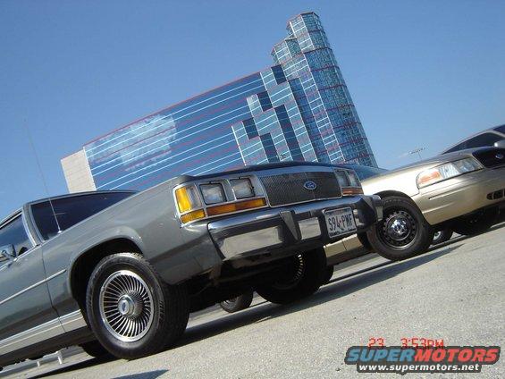 Gray 1988 Ford Crown Victoria LTD parked next to a gold Ford Crown Victoria with a modern glass building behind them