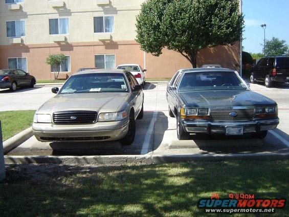 Two Ford Crown Victorias parked outside a hotel. One is tan, the other is dark gray