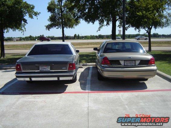 Two Ford Crown Victorias parked side-by-side, rear view. The car on the left is dark gray with a white roof. The car on the right is tan