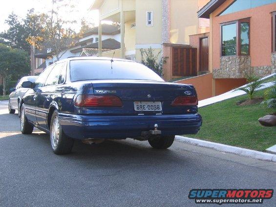 Rear view of a blue Ford Taurus parked on a street, with a second car visible behind it