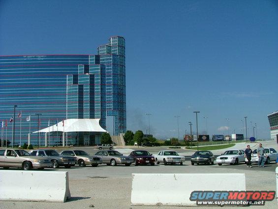 Several tan and silver Ford Crown Victorias parked in a lot with a modern building in the background