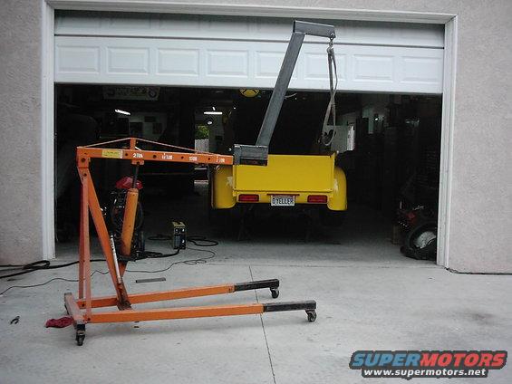 Yellow pickup truck bed with a license plate reading 'D YELLER' is suspended by an engine hoist inside a garage