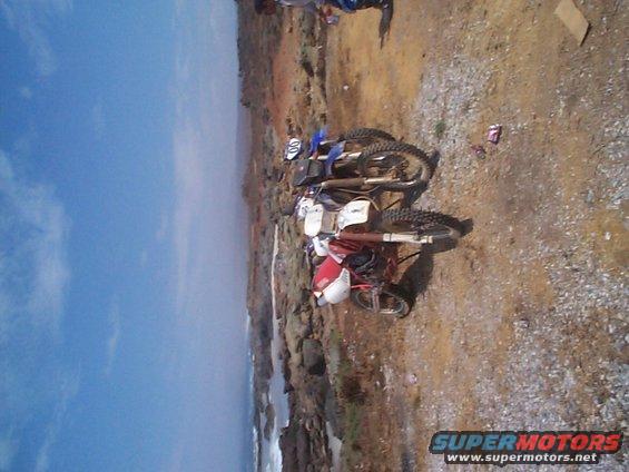 Two dirt bikes parked on a rocky, coastal terrain under a blue sky
