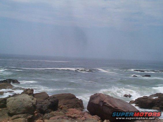 Rocky coastline with waves crashing against the shore under a cloudy sky