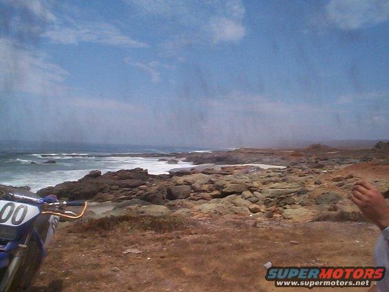 Blue motorcycle front plate with '00' visible, parked on a rocky coastline
