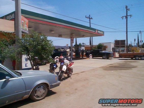 Several motorcycles and cars are parked at a PEMEX gas station under a covered canopy