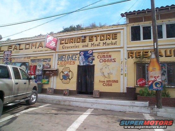 Silver pickup truck parked in front of a store with signs for 'Curios Store', 'Hielo-Ice Licores', and 'Cuban Cigars'