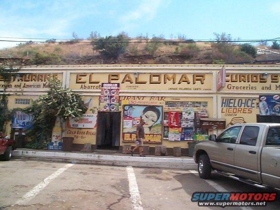 Tan pickup truck parked in front of a building with signs for "El Palomar" restaurant and bar