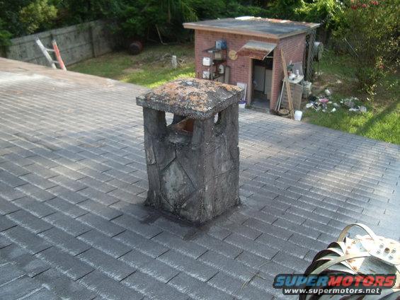 chimney on a shingled roof, with a brick shed in the background