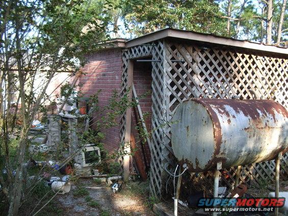 Rusty cylindrical fuel tank on stands next to a brick building with lattice work