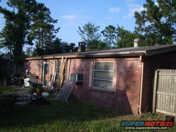 Backyard with a brick house, some clutter, and trees. There's a wooden fence on the right