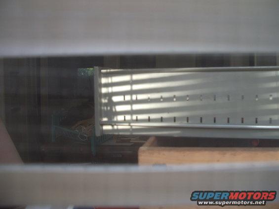 Metal grate with horizontal blinds casting shadows, seen through a window