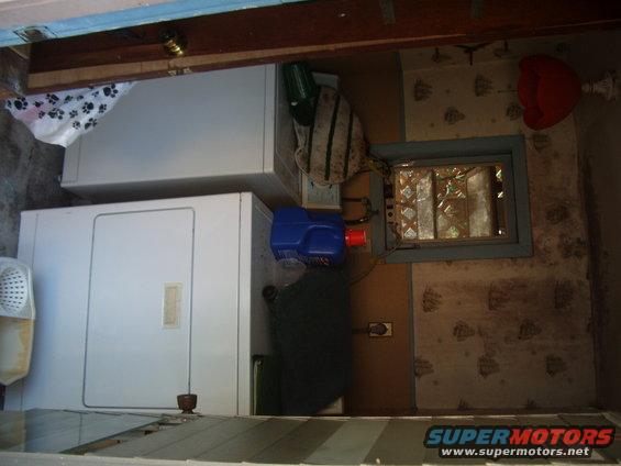 Laundry room interior with stacked white washer and dryer, blue detergent bottle, and small window