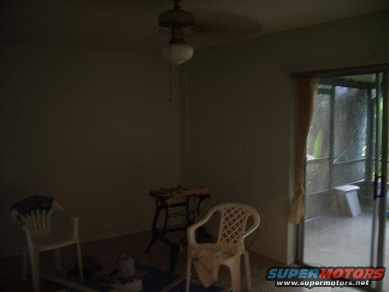 Interior room with two white plastic chairs, a sawhorse table, and a sliding glass door leading to a screened porch