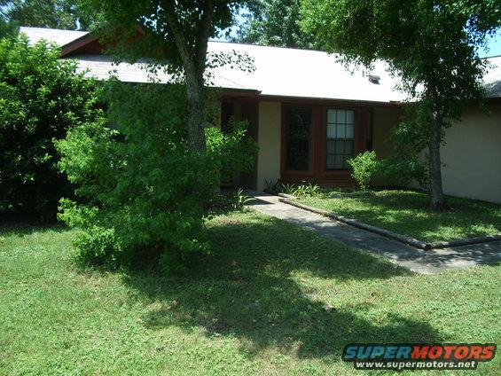 House exterior with a concrete walkway, grass lawn, and trees