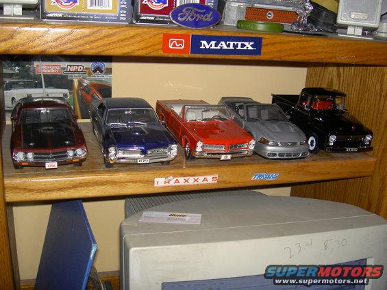 Collection of model cars including a red convertible and a black pickup truck on a wooden shelf