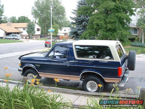 Dark blue Ford Bronco with tan lower trim and a white removable top, parked curbside