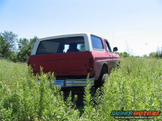 Red SUV parked in a field of tall green grass under a clear blue sky