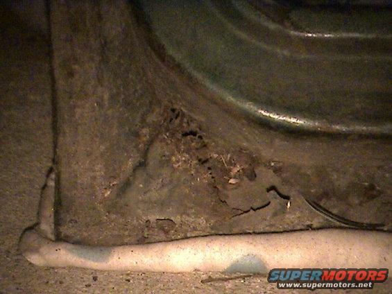 Close-up of heavily rusted metal panel with holes and cracks, showing a curved surface