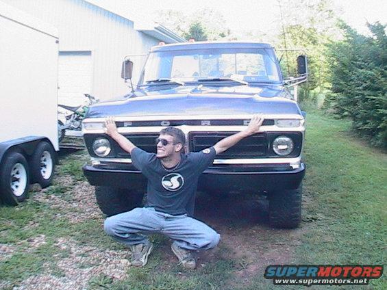 Blue Ford F-Series truck with a man squatting in front of its grille