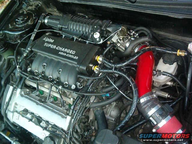 Engine bay with Alpine supercharger and red intake pipe. Text reads 'Alpine SUPER-CHARGED AQUA-COOLED'