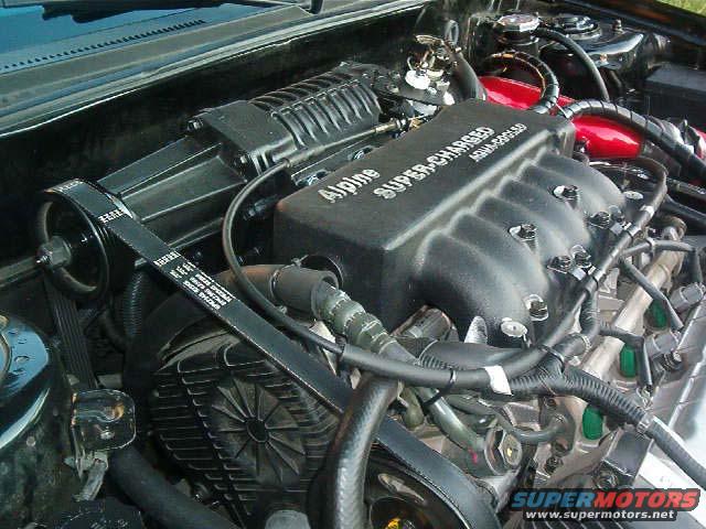Close-up of a supercharged engine with an Alpine intake manifold. Drive belt and pulleys visible