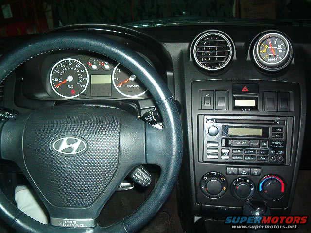 2003 Hyundai Tiburon interior showing dashboard, steering wheel with Hyundai logo, and aftermarket gauge