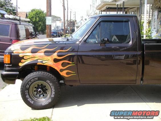 Side view of a brown 1991 Ford F-150 pickup truck with orange and yellow flame decals on the fender and door