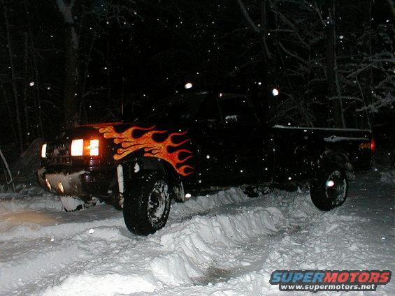 Black pickup truck with flame decals stuck in deep snow at night
