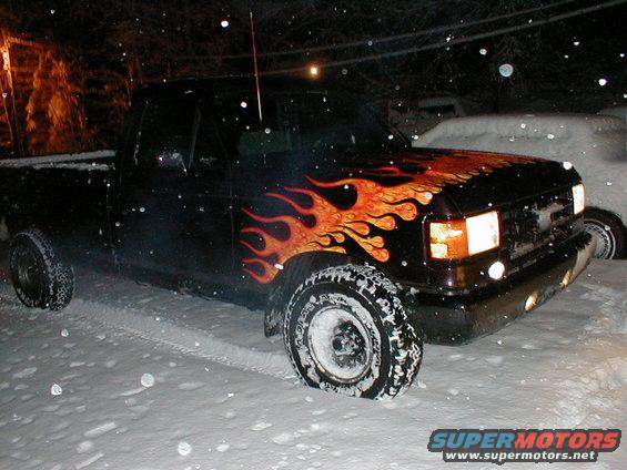 Black pickup truck with flame decals on the hood and fender, parked in snow