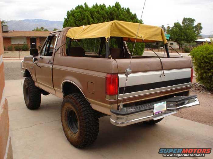 1989 Ford Bronco with a tan soft top, lifted suspension, and large tires, parked in a driveway