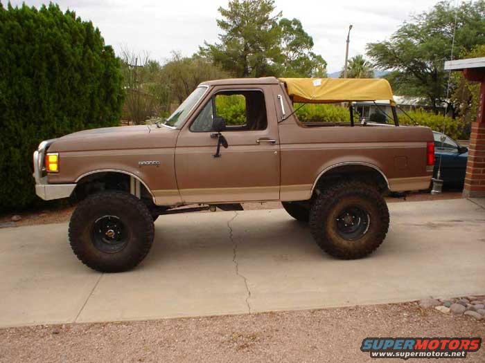 Brown 1989 Ford Bronco with a yellow soft top over the rear bed, lifted with large tires