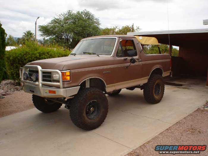 Brown Ford Bronco with a brush guard and a yellow soft top, parked in a driveway next to a garage