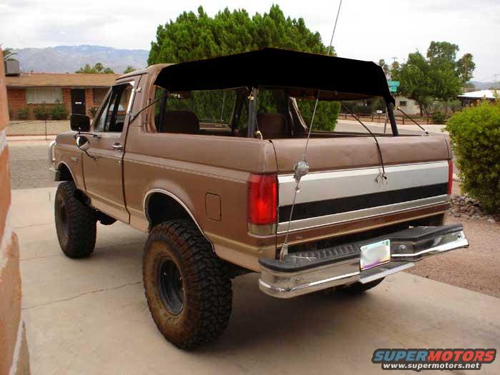 Brown 1989 Ford Bronco with a black soft top, lifted suspension, and off-road tires