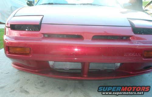 Front view of a red 1990 Nissan 240SX with pop-up headlights and an aftermarket intercooler visible