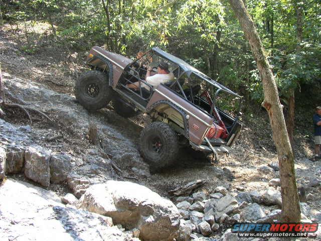 Brown Ford Bronco with roll cage climbing a rocky hill