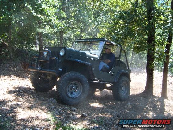 Green Jeep CJ-5 driving on a dirt trail through trees