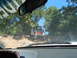 1988 Ford Bronco - Two vehicles navigate a challenging off-road trail surrounded by trees under a clear blue sky.