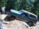 1988 Ford Bronco - A green Ford Bronco navigates a challenging off-road trail with a person watching.