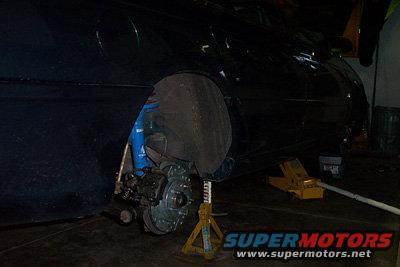 Car's front wheel assembly removed, supported by a jack stand. Blue shock absorber visible