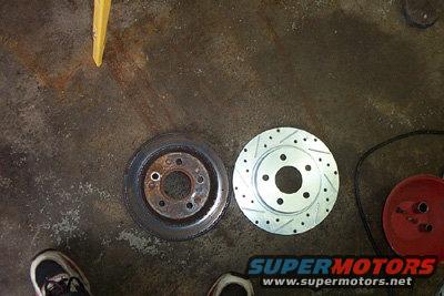 Two brake rotors, one rusty and used, the other new and slotted, lie on a concrete floor