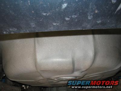 Underside view of a vehicle's fuel tank and frame. SuperMotors.net logo visible