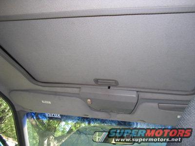 Car interior showing the sunroof and overhead console. Trees visible through the windshield